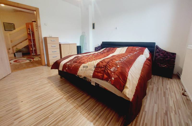 A bedroom in a family house with a double bed, a wooden-patterned floor, and a dresser.