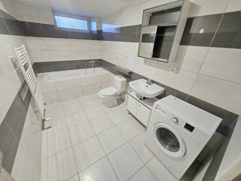 A bathroom in a 3-room apartment with a washing machine, bathtub, and tiles.