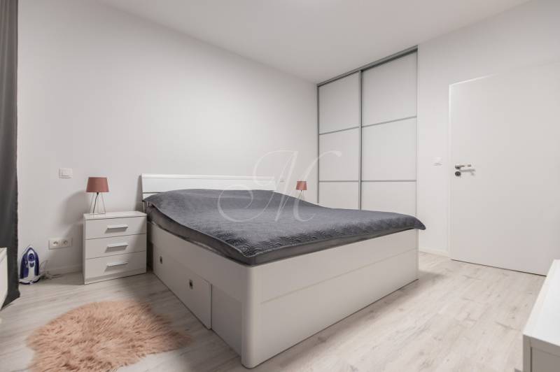 A bedroom with white furniture, a double bed, and a floor with a wood decor in a two-room apartment.