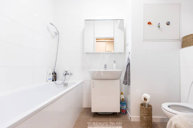 Bathroom in a 2-room apartment with a bathtub, sink, and toilet, white tiles combined with a brown floor.
