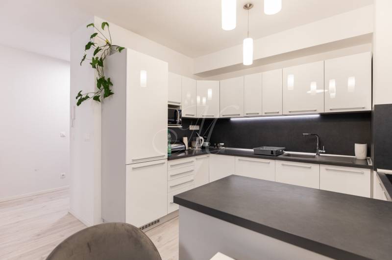 A kitchen unit with white cabinets and a black countertop in a two-room apartment.
