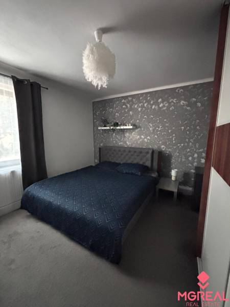 A bedroom with dark bedding, gray walls, and a designer lamp in a two-room apartment.