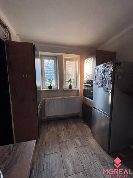 Kitchen in a 2-room apartment with three windows, tiles, and kitchen cabinets.
