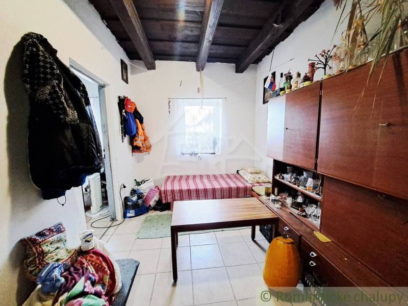 Interior of a family house with a wooden ceiling, furniture, bed, and clothes on the wall.
