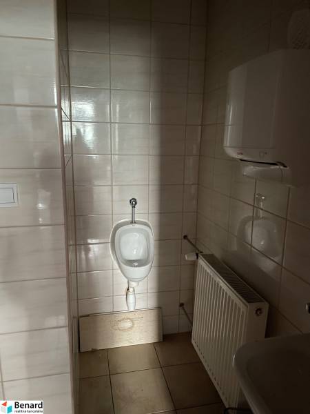 A restroom in commercial premises with tiles, a radiator, and a urinal.