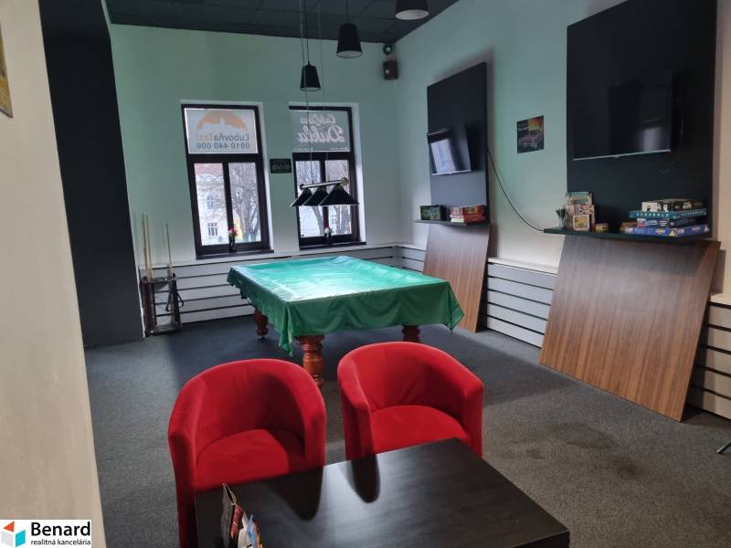 Commercial space with a pool table, red armchairs, and a table with games.