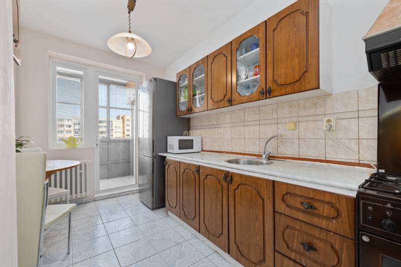 A kitchen with a wooden cabinet and appliances in a 3-room apartment with access to a balcony.