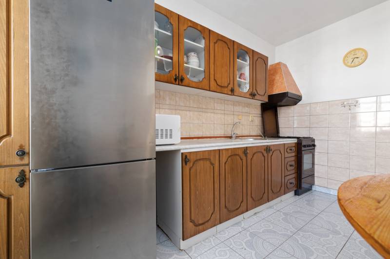 A kitchen in a 3-room apartment with wooden cabinets, a microwave, and a stainless steel refrigerator.
