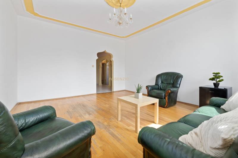 Living room in a three-room apartment with green sofas and wooden flooring.
