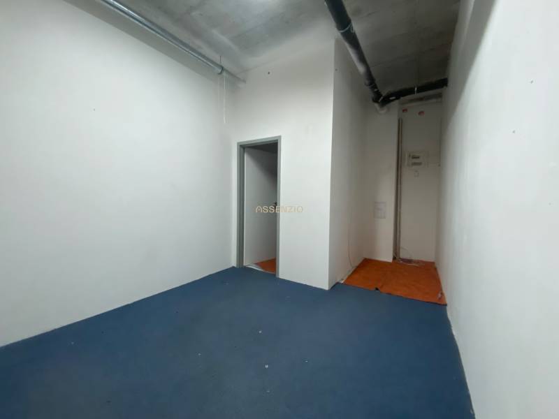 Commercial space with blue carpet, white walls, and piping on the ceiling.