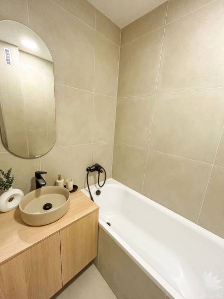 A bathroom in a 4-room apartment with a bathtub, sink, and mirror in beige tones.