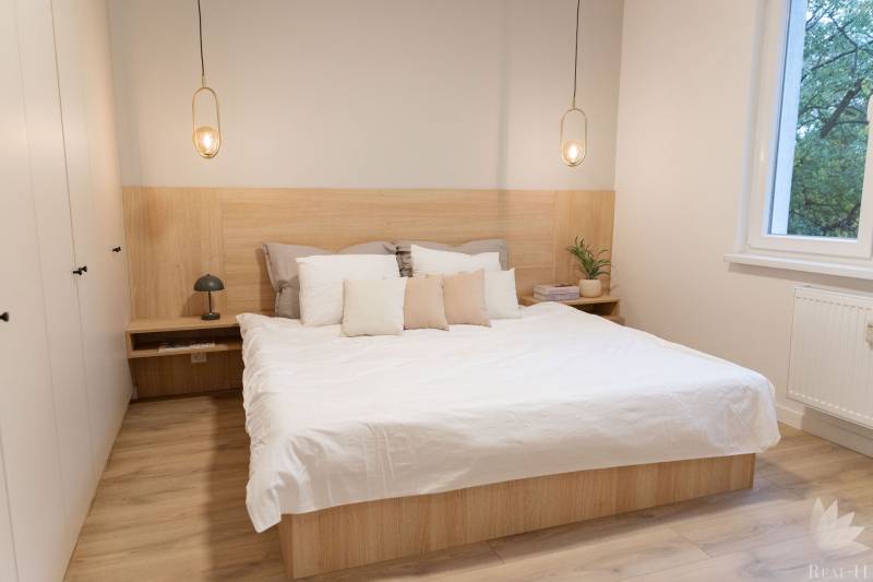 A bedroom with light furniture, pendant lights, and a wood-patterned floor.