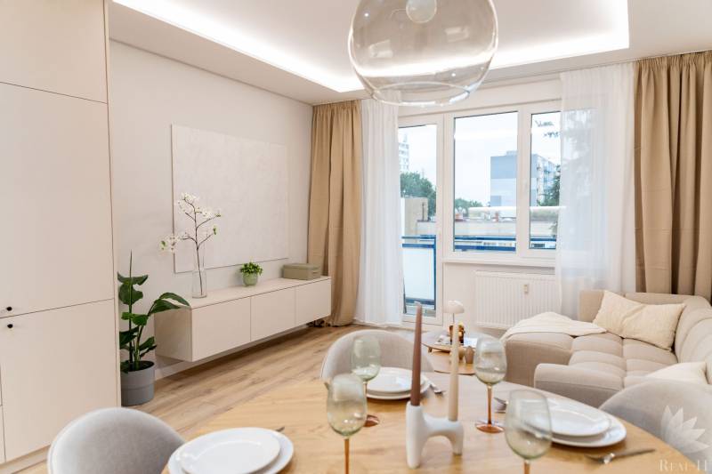 Living room of a 4-room apartment with a large window, beige sofa, and dining table.