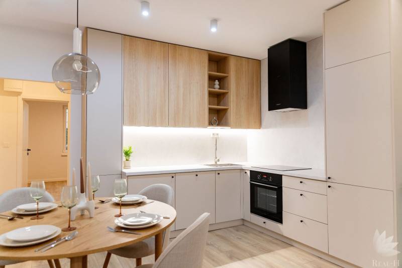 A kitchen in a 4-room apartment with white cabinets, wooden cupboards, and a small dining table.
