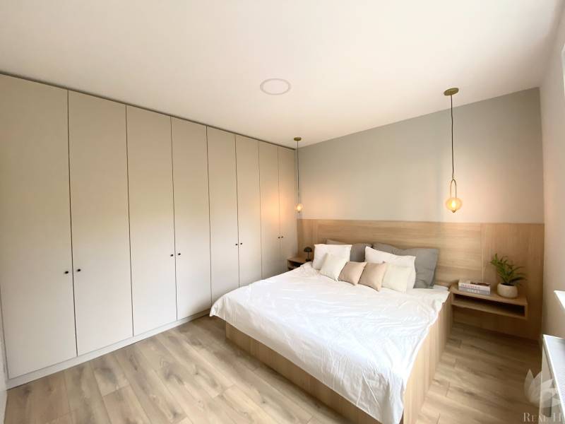 A bedroom in a 4-room apartment with a white bed, wardrobes, and a floor with a wooden decor.