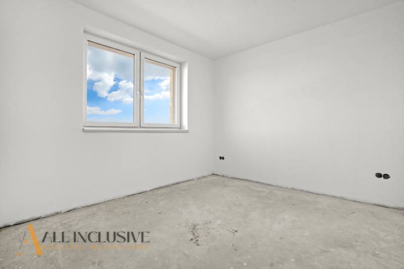 A spacious room in a family house with white walls and a window overlooking the sky.