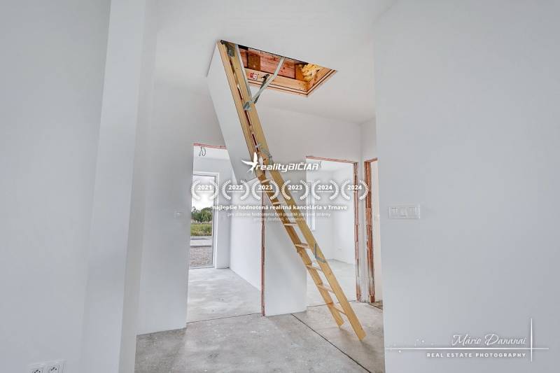 White interior of a family house with built-in attic stairs and gray flooring.