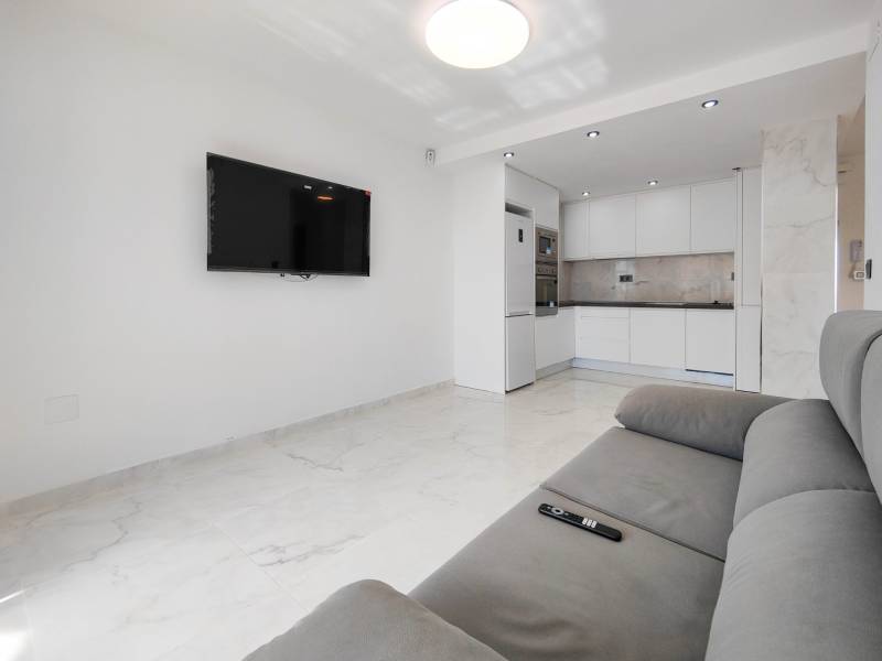 Living room with a TV and kitchen in a 3-room apartment with white walls.
