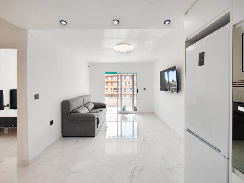 Living room of a 3-room apartment with a marble floor, sofa, and a TV on the wall.