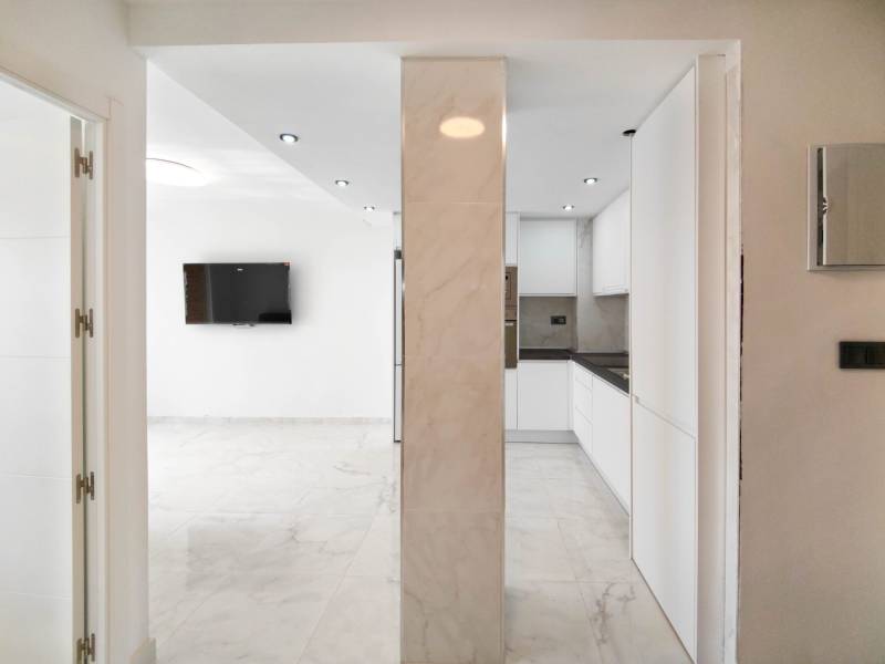 Kitchen area and living room in a 3-room apartment with tiles and a TV on the wall.