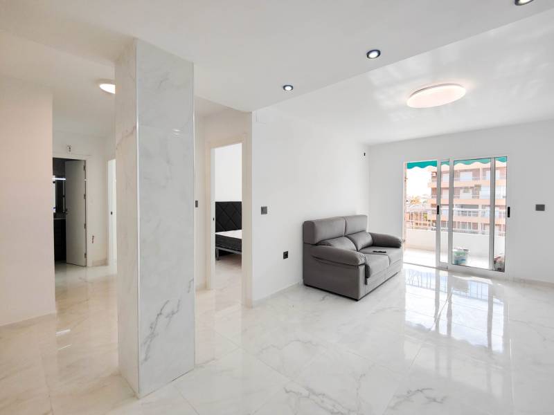Living room in a three-room apartment with tiles and a couch, illuminated by large windows.
