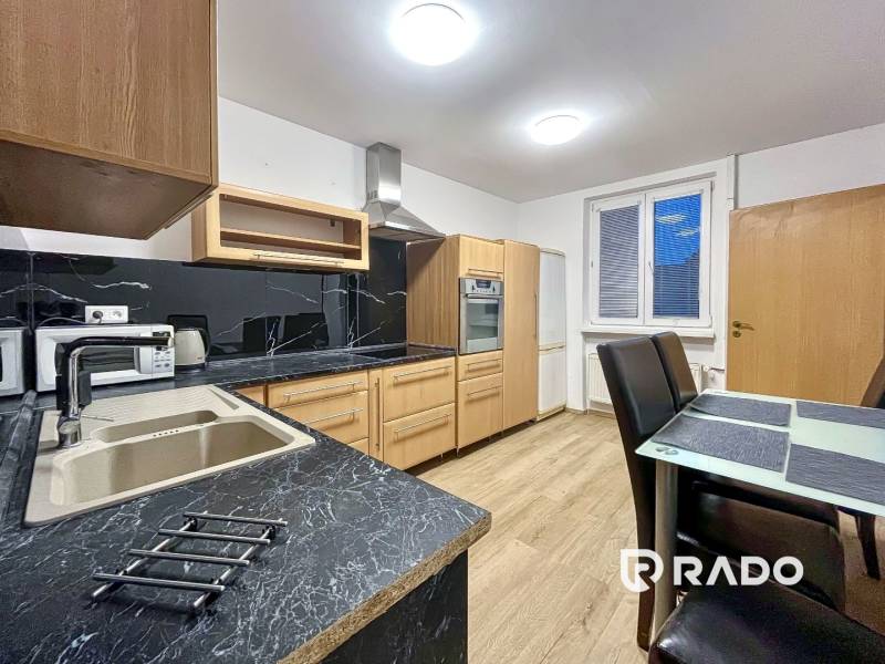 A kitchen in a 2-room apartment with a wooden decor floor and black countertops.