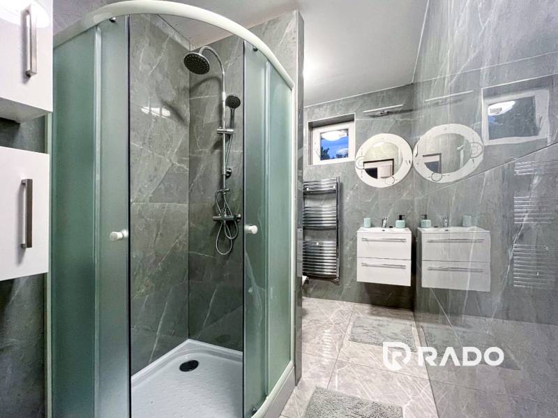 A bathroom in a 2-room apartment with ceramic tiles, a shower corner, and two sinks.