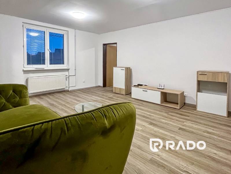 Living room in a two-room apartment with a wooden decor floor, a green sofa, and modern furniture.