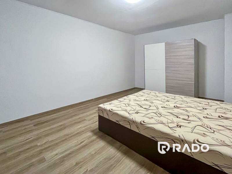 Bedroom in a two-room apartment with a bed, wardrobe, and wooden decor flooring.