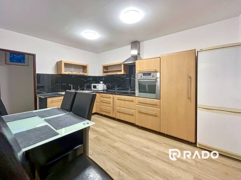 A kitchen with a wood-patterned floor in a 2-room apartment with appliances and a dining table.