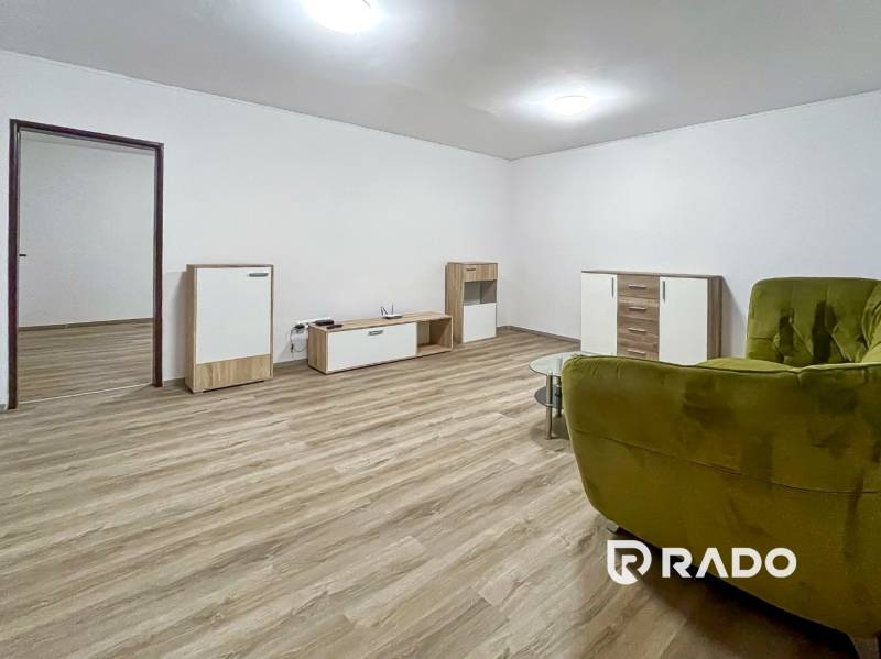 Living room of a two-room apartment with a wooden decor floor and a green armchair.