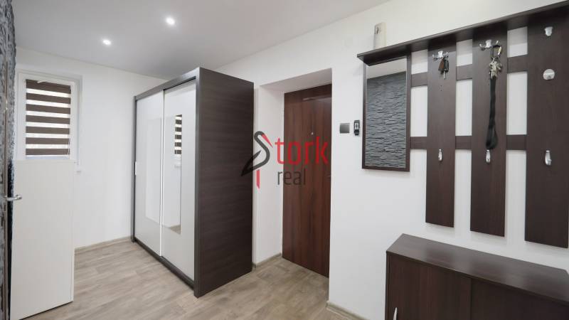 A hallway in a 2-room apartment with a mirrored wardrobe and a wooden decor floor.