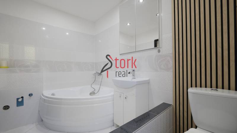 Bathroom with a bathtub and a sink in a 2-room apartment with a wooden decor on the wall.