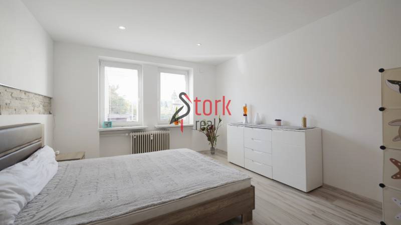 Bedroom in a 2-room apartment with wood-patterned flooring, white furniture, and a decorative wall.