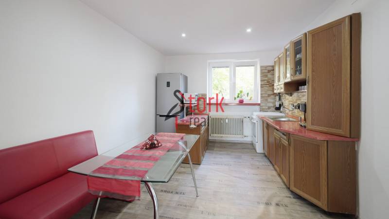 A kitchen in a 2-room apartment with a wooden decor floor and red seating.