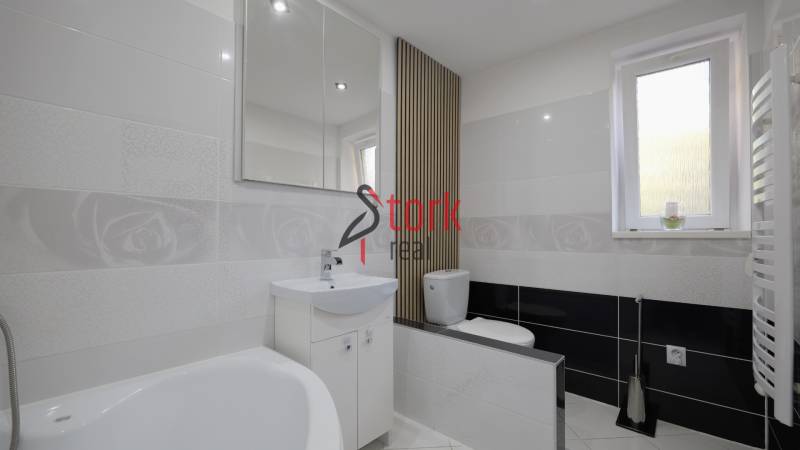 Bathroom in a 2-room apartment with light tiles, a bathtub, and a large mirror.