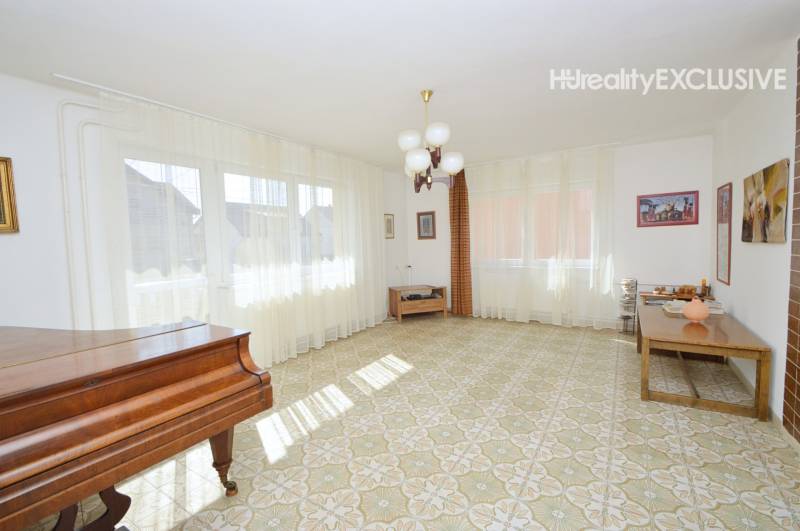 Living room in a family house with a piano, curtains, and a table on a tiled floor.