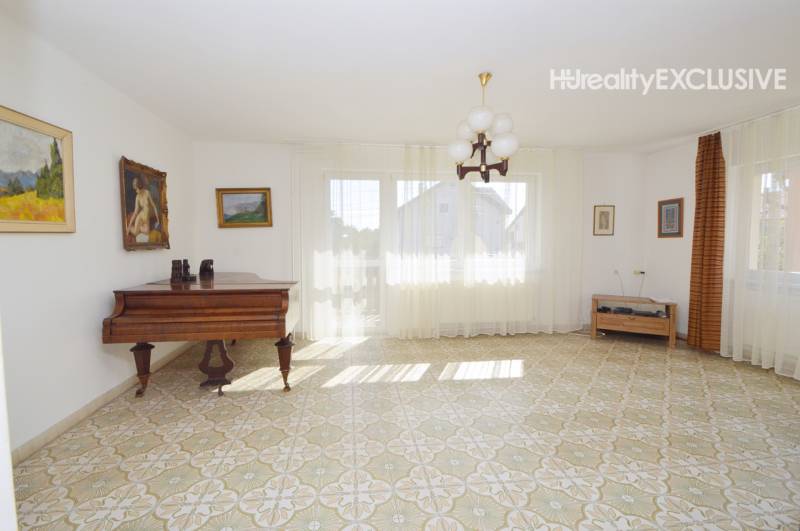Living room with a piano, patterned floor, and paintings in a family house.