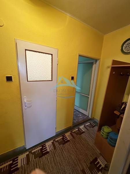 Hallway in a 2-room apartment with yellow walls, white doors, and a colorful carpet.