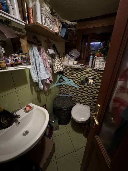 A small bathroom in a cottage with a sink, toilet, tiles, and a lot of toiletries.