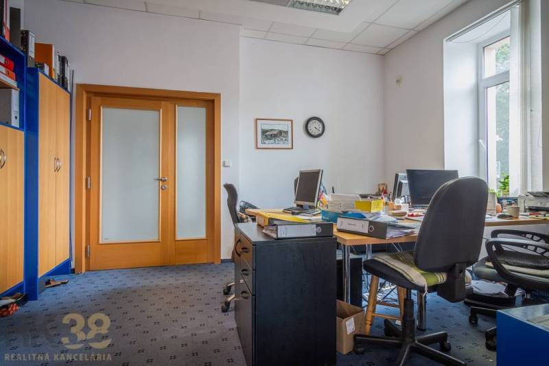 Office in a building with carpet, with various cabinets and a desk under the window.