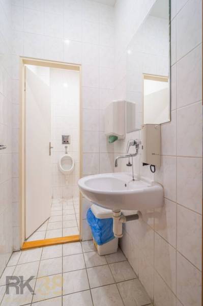 A bathroom in a building with a sink, mirror, and urinal, visible tiles.