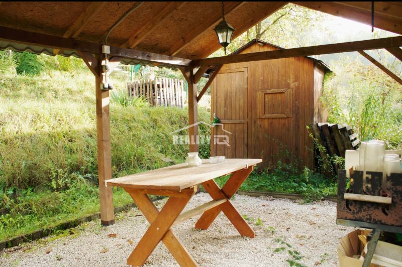 Covered terrace with a table in the garden in Budatín, Žilina, next to a wooden cottage.