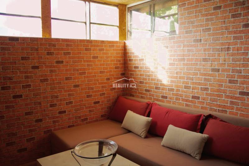 Red brick walls with a sofa and cushions in the Garden area.