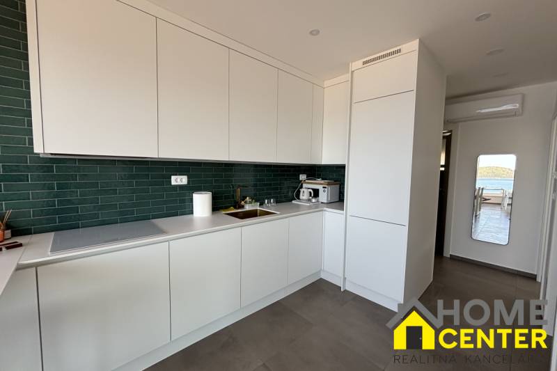 A kitchen in a villa with white cabinets, green tiles, and a view of the terrace.