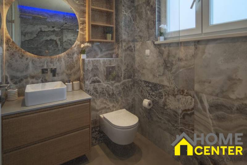 A bathroom in a villa with modern elements, marble tiles, a wall-hung toilet, and a sink.