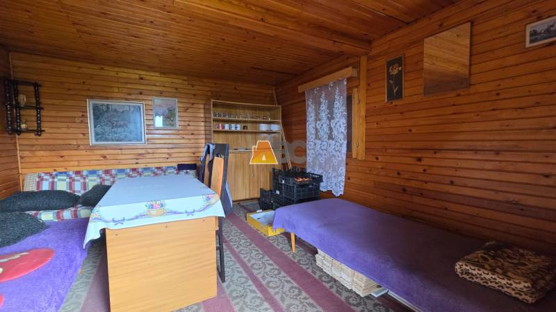 Interior of a garden with wooden paneling, a sofa, and a table with a cover.