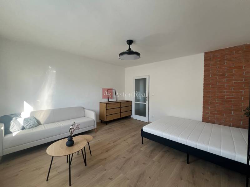 Living room with a sofa, table, and bed, floor with wooden decor.