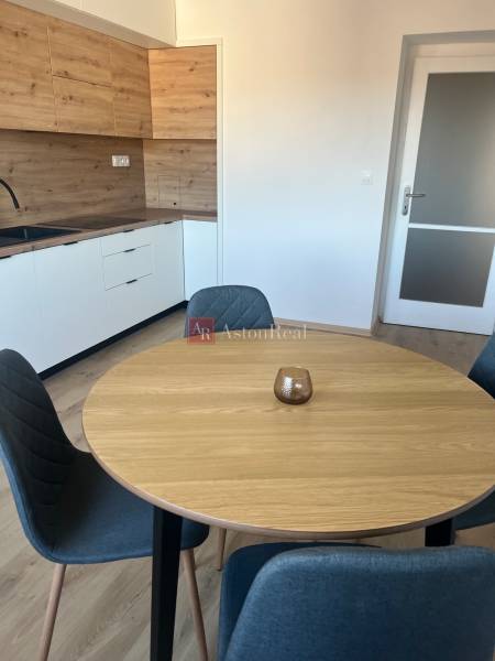 A kitchen in a studio apartment with a wooden-patterned floor and a modern dining table.