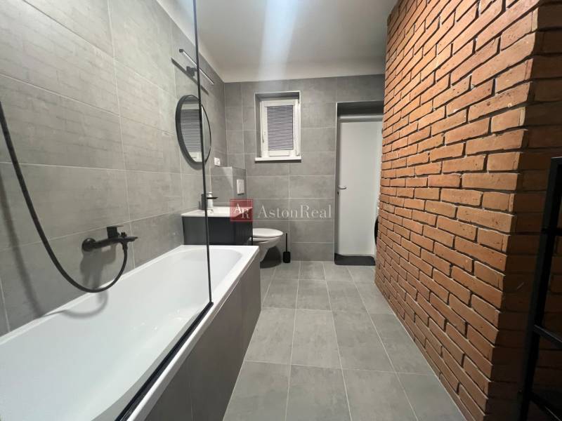 Bathroom in a studio apartment with a brick wall and gray tiles.